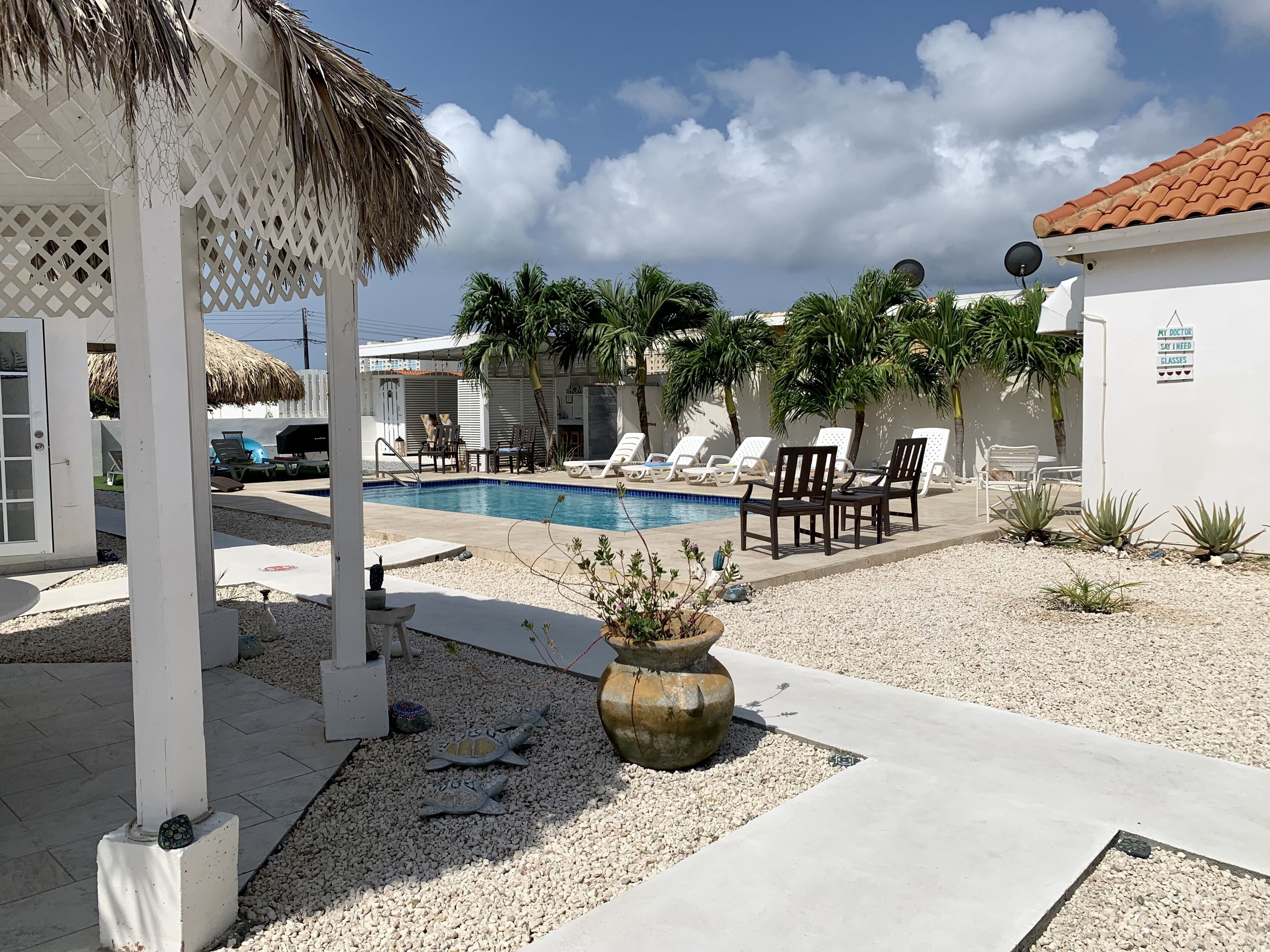 A pool area with lounge chairs, a thatched roof structure, and a sign on a wall.