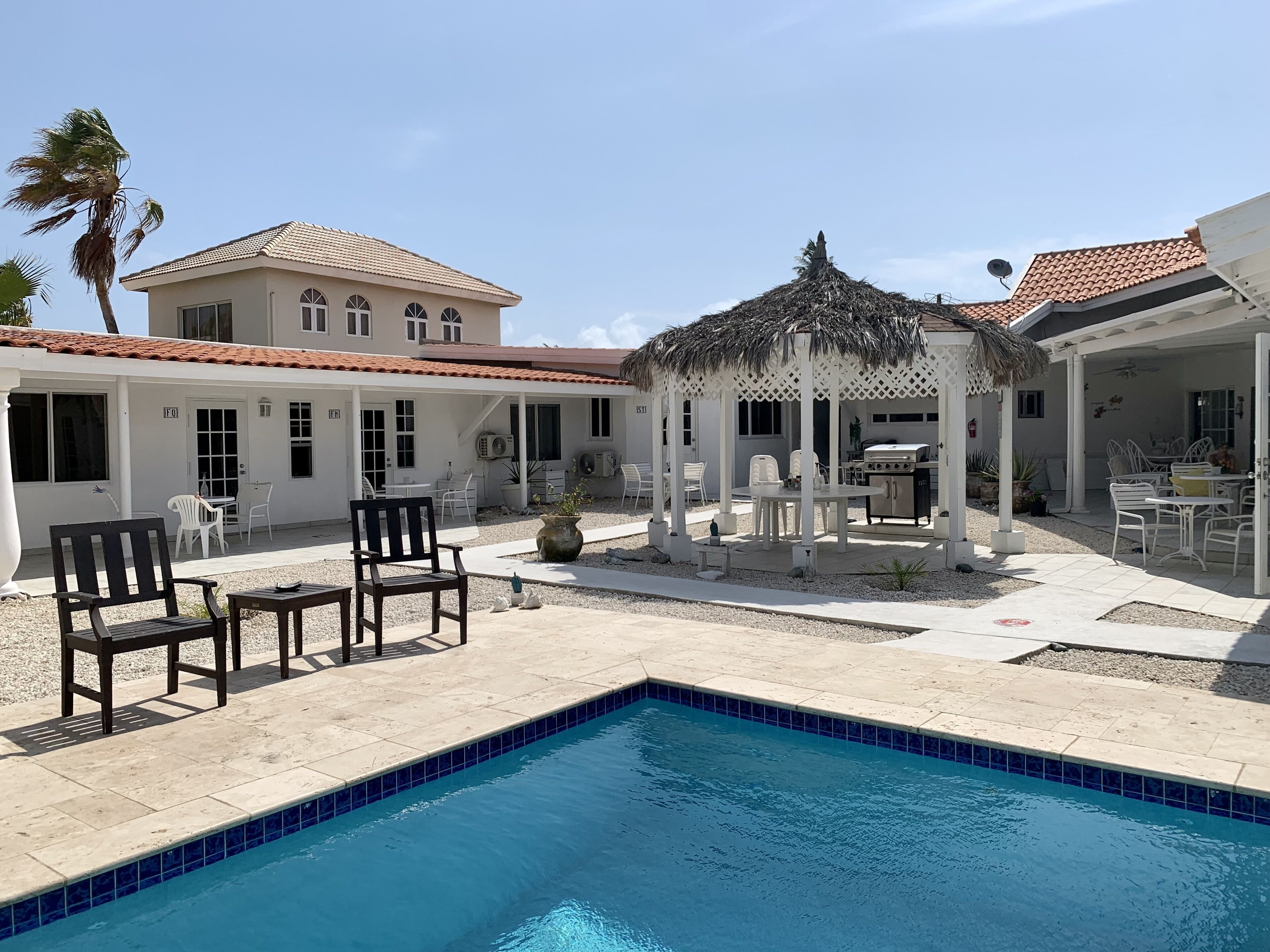 A pool area with a gazebo, outdoor seating, and a building with a tiled roof.