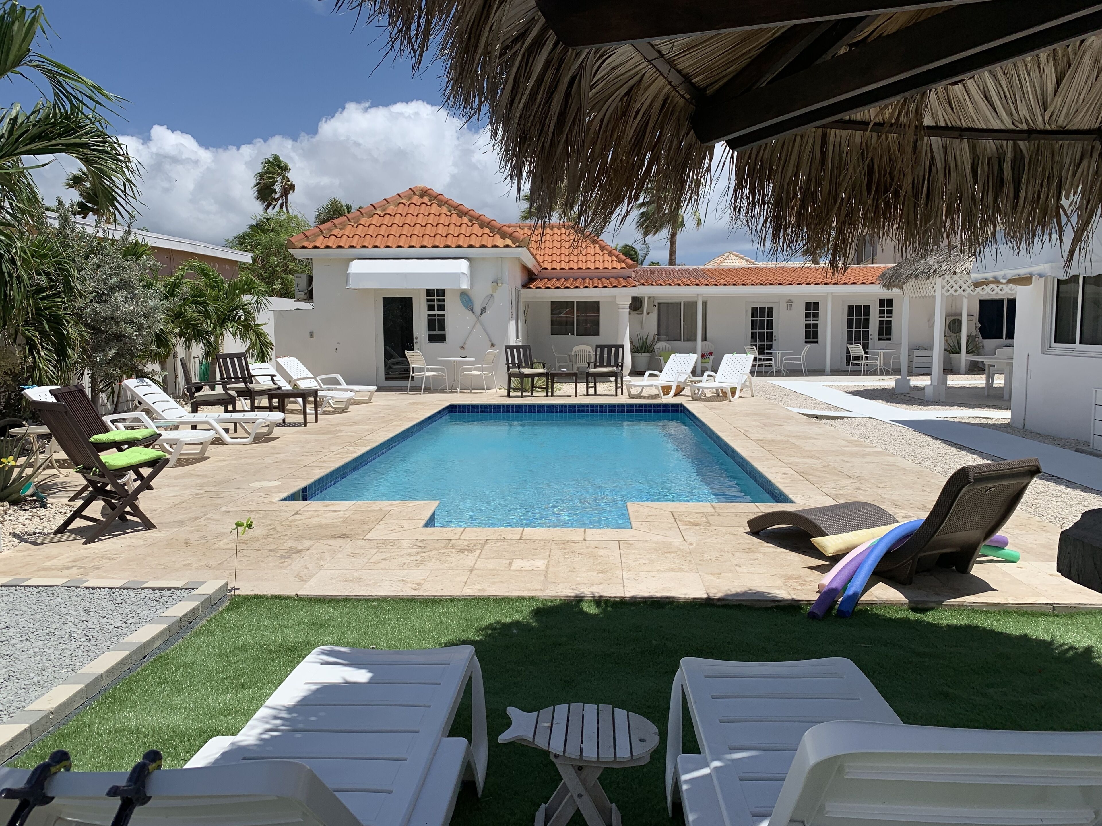 A pool area with lounge chairs, a small pool, and a building with a tiled roof.