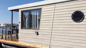Une maison flottante moderne dotée d’une grande fenêtre et d’un petit espace extérieur avec des chaises.