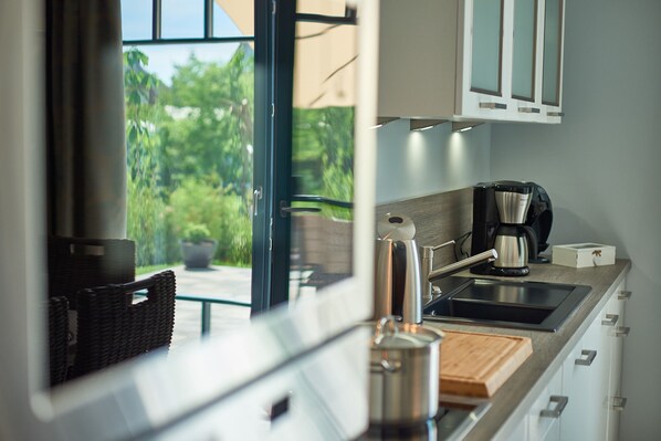 A modern kitchen with a large window, a coffee maker, and a cutting board on the counter.