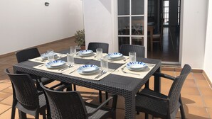 A dining area with a table set for four, surrounded by wicker chairs, and a sliding glass door leading to an indoor space. - GREAT CENTRAL HOUSE TIAS LANZAROTE (Tías)