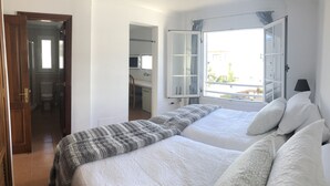A bedroom with two beds, a window with curtains, a door, and a view of the outside. - GREAT CENTRAL HOUSE TIAS LANZAROTE (Tías)