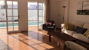 A spacious living room with a large sliding glass door leading to a pool area, a comfortable sofa, and a coffee table. - GREAT CENTRAL HOUSE TIAS LANZAROTE (Tías)