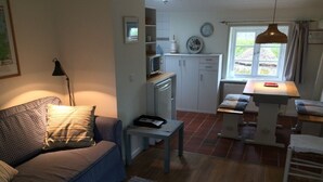 A compact living space with a sofa, a small table, a kitchen area with cabinets, a dining table, and a window with a view. -  New: Apartment Mühlenblick, balcony and garden, WiFi (Struckum)