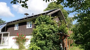 A house with a sloped roof, solar panels, and a garden with a large bush and red flowers. -  New: Apartment Mühlenblick, balcony and garden, WiFi (Struckum)
