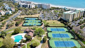 Un resort con varias canchas de tenis, piscina y vistas a la playa.