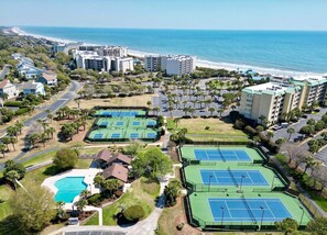 Een resort met meerdere tennisbanen, een zwembad en uitzicht op het strand.