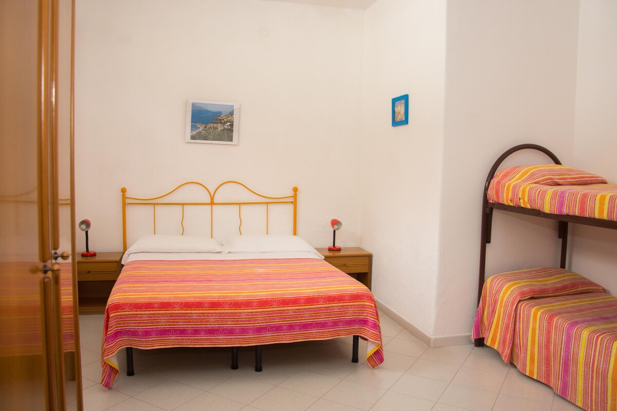 A room with a single bed, a bunk bed, a bedside table with a lamp, and a framed picture on the wall.