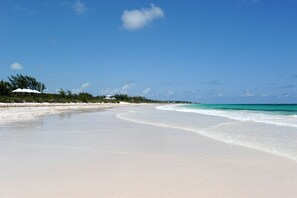 A beach with white sand, clear turquoise water, and a few trees in the background.