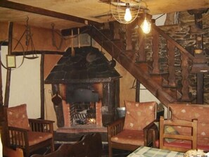 A rustic interior with a stone fireplace, wooden chairs, and a checkered tablecloth. - Rural house (full rental) Carriles Romanos for 8 people (Castrillo de Cabrera)
