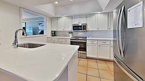 A modern kitchen with white cabinetry, stainless steel appliances, and a large island with a sink. - Marshfront 14E Beautiful View, Beach & Pool! (Pawleys Island)