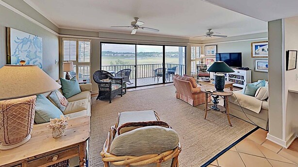 A spacious living room with a large sliding glass door leading to a balcony, a ceiling fan, and a television. - Marshfront 14E Beautiful View, Beach & Pool! (Pawleys Island)