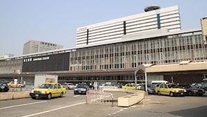 Een modern gebouw met een grote glazen gevel, een bord waarop “SHIN-OSAKA STATION” staat, en verschillende gele taxi’s die ervoor geparkeerd staan.