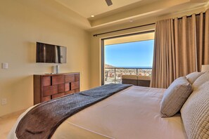 A bedroom with a large bed, a TV mounted on the wall, a wooden dresser, and a balcony with a view. - Golf Resort Condo w/ Ocean Views at Cabo Quivira (Cabo San Lucas)