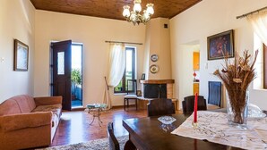 Een woonkamer met een bank, een eettafel met stoelen, een open haard en een kroonluchter.
