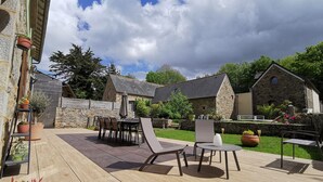 An outdoor patio area with a wooden deck, a table with chairs, and a stone building in the background. - Country house by the sea - Perros Guirec on the Pink Granite Coast (Saint-Quay-Perros)