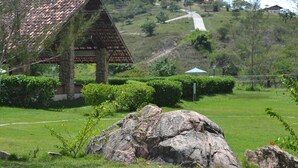 Un bâtiment rustique, doté d’un toit en tuiles, entouré de pelouses et d’arbustes bien entretenus, se dressant sur un terrain vallonné sous un ciel dégagé.