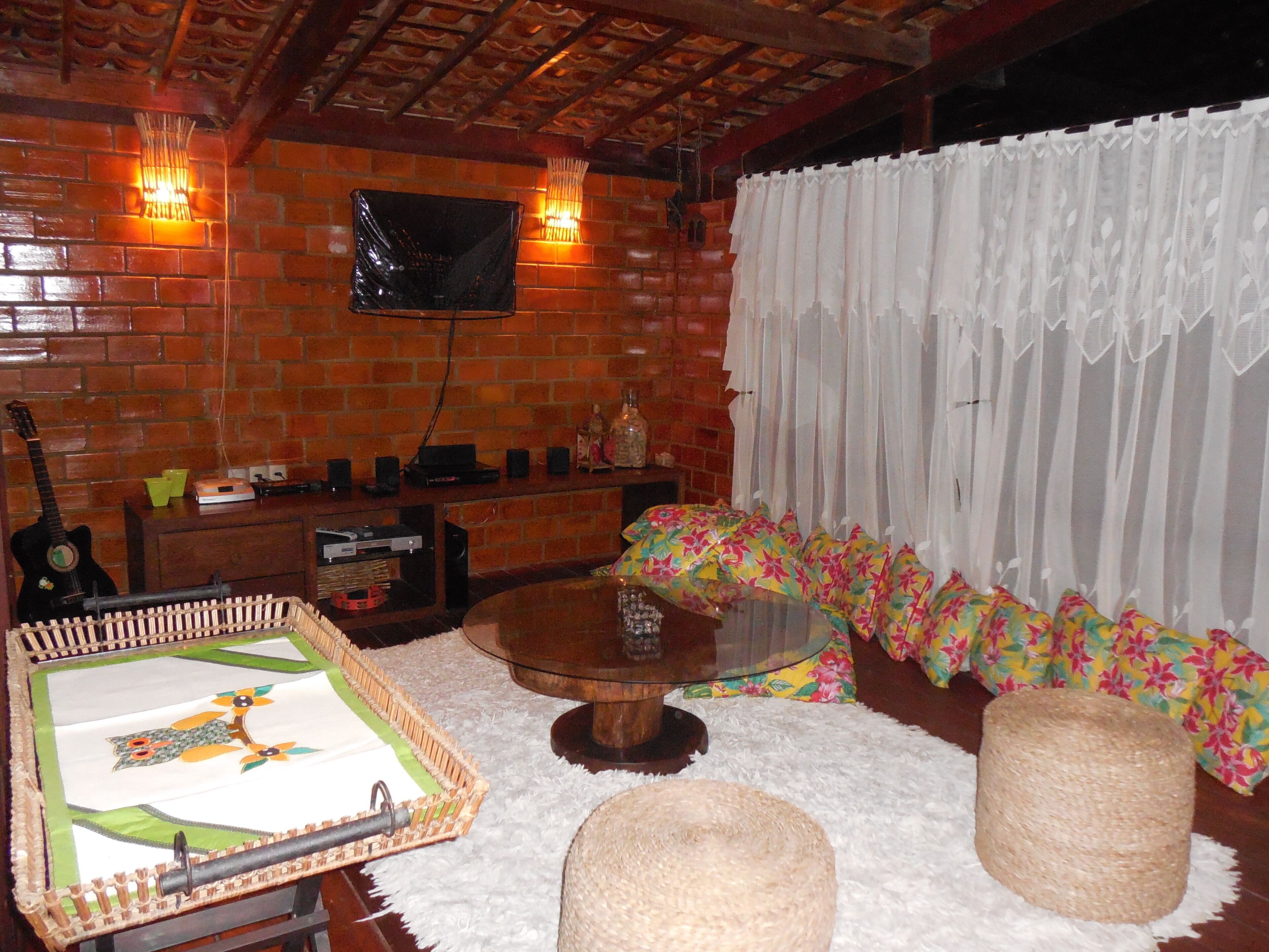 Una habitación acogedora con pared de ladrillo, un televisor de pantalla plana sobre un mueble de madera, una guitarra y una mesa con una cesta tejida.