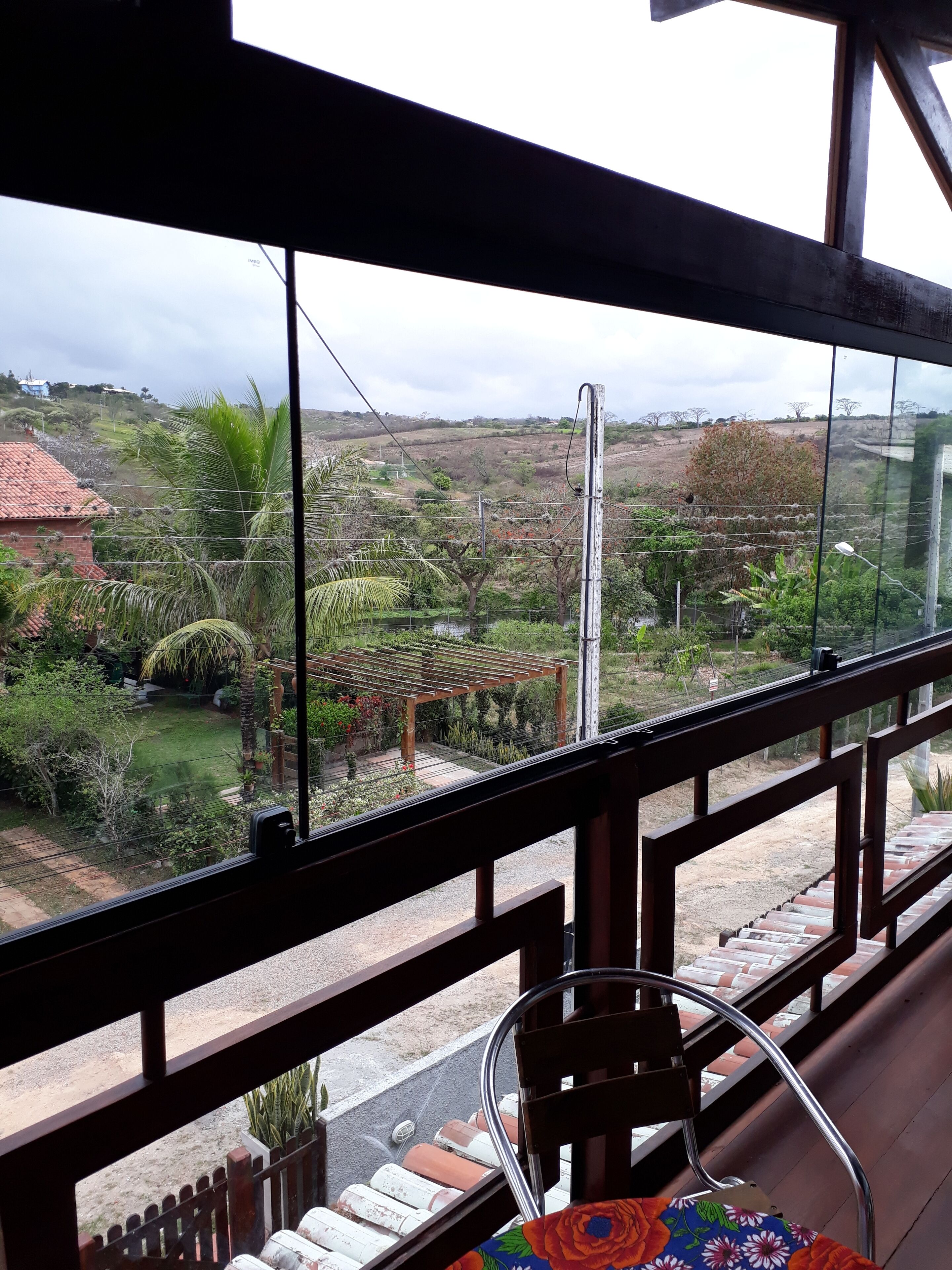 A view from a balcony with a wooden railing, a chair, and a table with a colorful tablecloth.