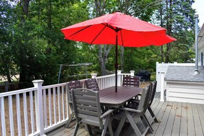 A deck with a table and chairs, a red umbrella, and a white railing. - Charming 3-Bedroom Getaway Just 1 Mile from Sea Street Beach – Dennisport (Dennis Port)