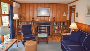 Ein gemütliches Wohnzimmer mit Kamin, Bücherregalen, einem blauen Sofa und einer Holzwand.