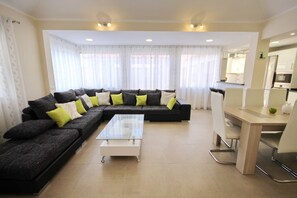 A modern living room with a sectional sofa, a glass coffee table, and a dining area with a white table and chairs.