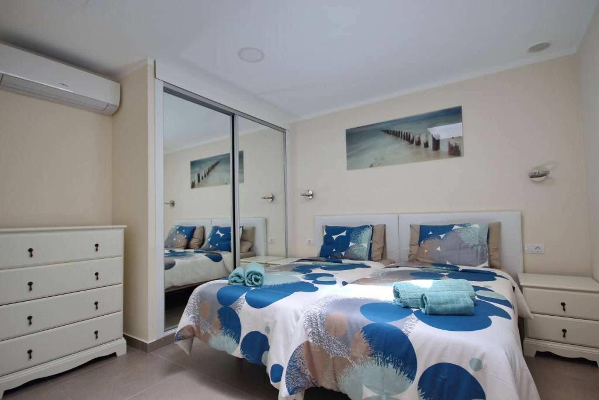 A bedroom with a bed, a dresser, a nightstand, a mirror, and a wall-mounted picture.