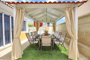 A covered outdoor dining area with a table and chairs, surrounded by curtains, and a view of the outside.