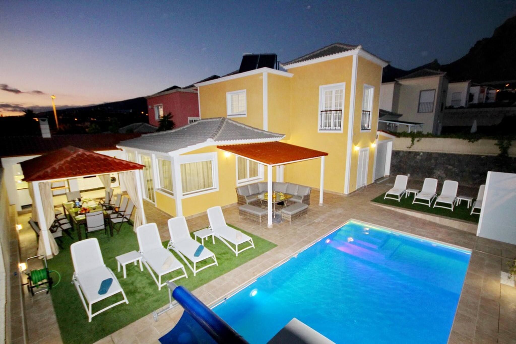 A swimming pool with lounge chairs and umbrellas, surrounded by a house with a patio.