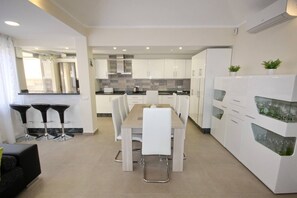 Een moderne keuken met witte kasten, een eettafel met stoelen en een koelkast met wijnglazen bovenop.