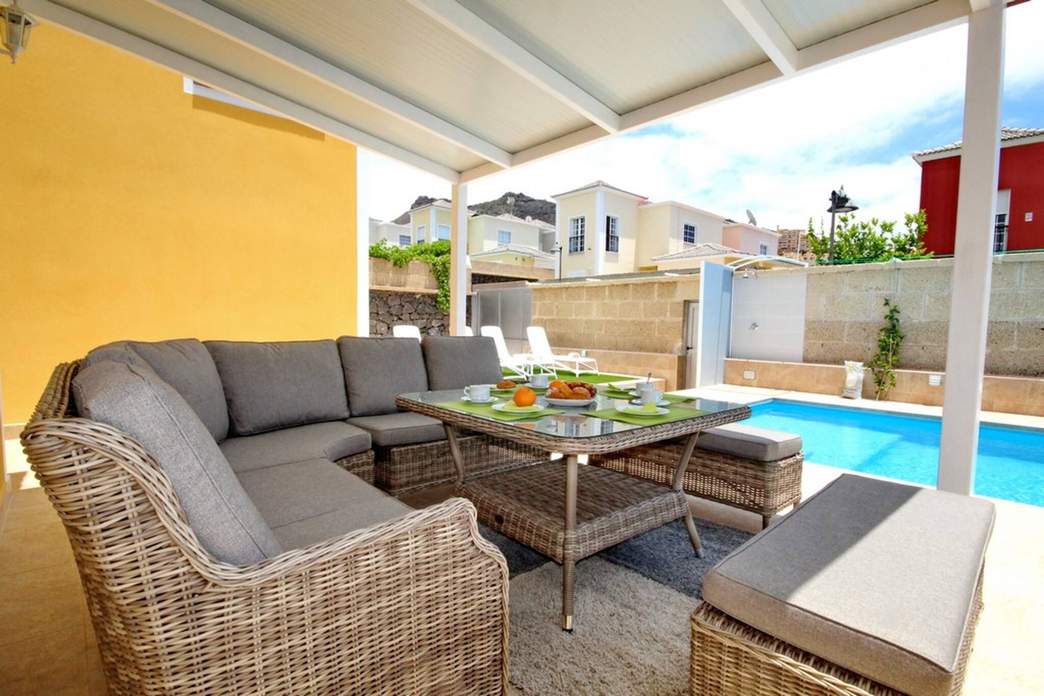 Un espace extérieur abrité, aménagé avec une piscine, des meubles en osier et une table dressée pour les repas.