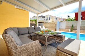 Un'area salotto esterna coperta con piscina, mobili in vimini e un tavolo apparecchiato per mangiare.