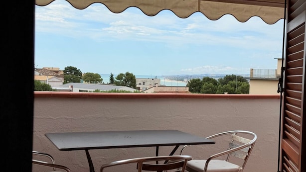 An outdoor balcony with a table and chairs, a view of the sea, and buildings in the background. - N096 - Numana, two-room villa with garden and sea view (Sirolo)