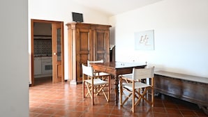 A dining area with a wooden table and chairs, a kitchen in the background, and a white wall with a framed picture. - N096 - Numana, two-room villa with garden and sea view (Sirolo)