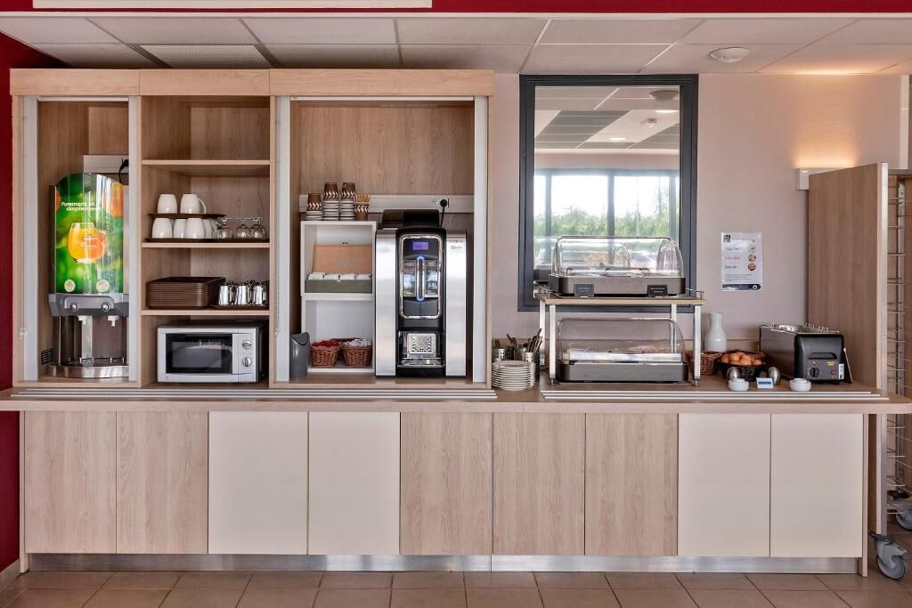 A self-service breakfast area with a coffee machine, microwave, toaster, and a display case with food items.