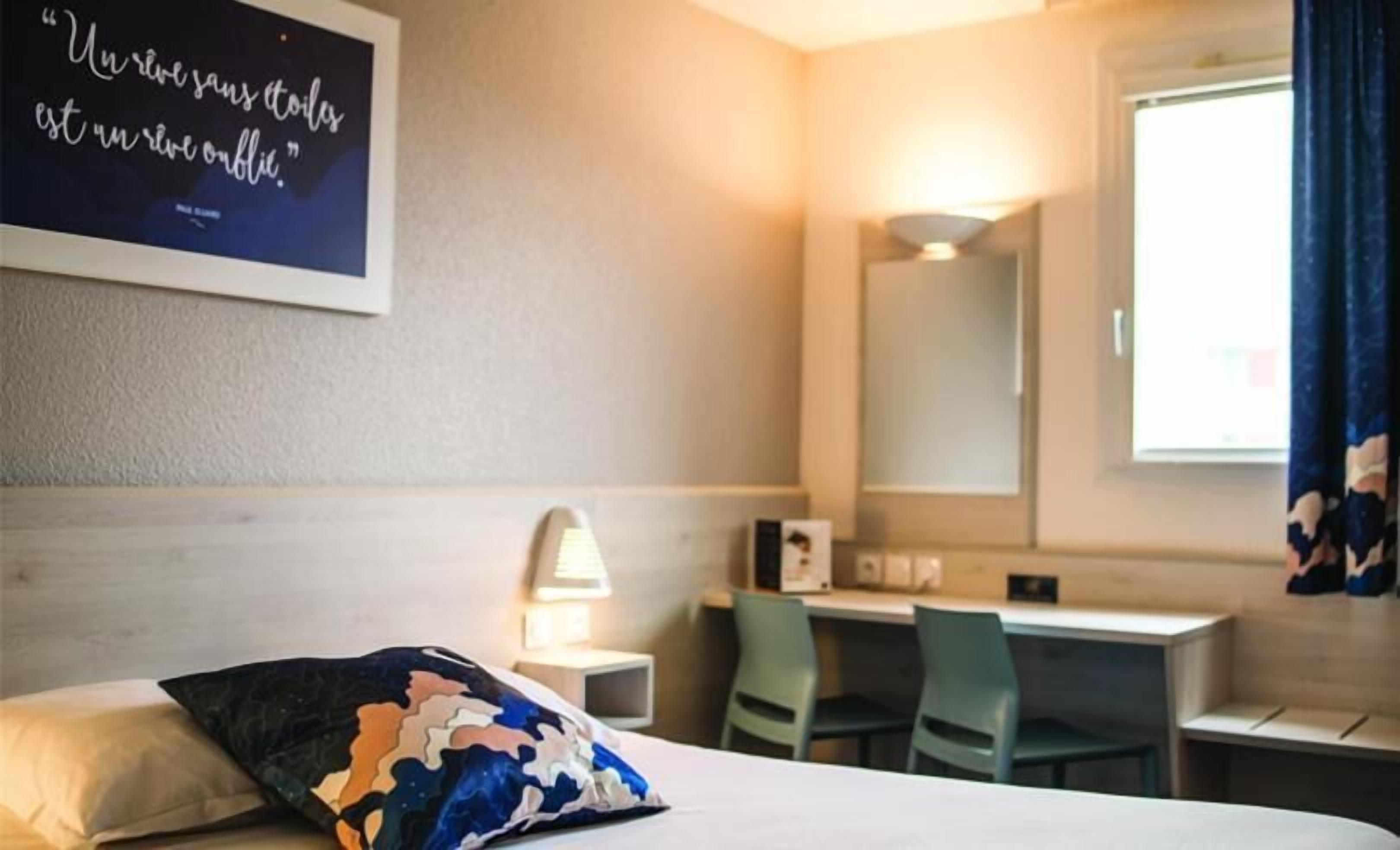Habitación de hotel con cama, escritorio, silla, lámpara y un espejo grande.