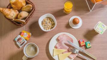 A breakfast table with croissants, cereal, orange juice, eggs, ham, cheese, coffee, butter, and condiments.