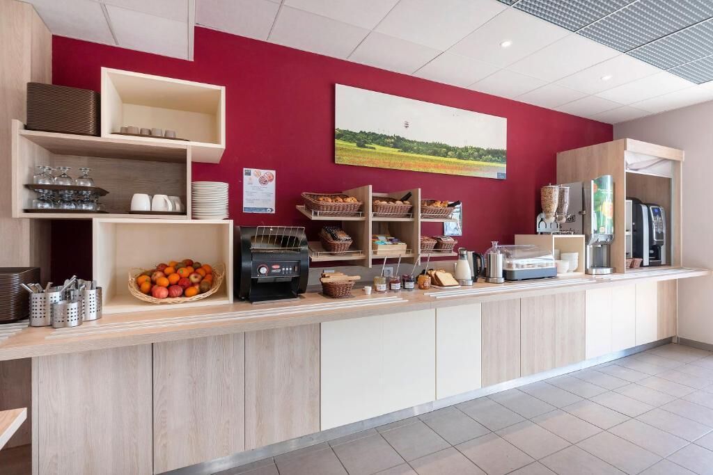 A modern reception area with a red wall, a coffee machine, and various food items on display.
