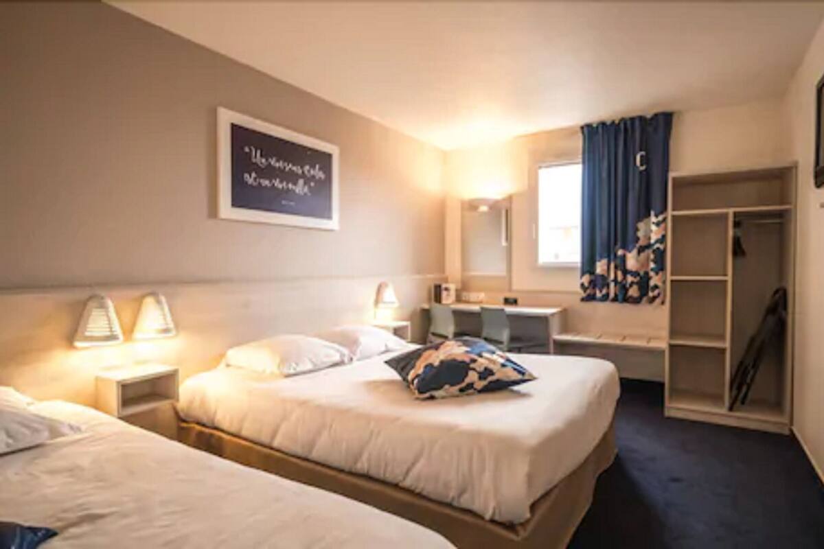 A hotel room with two beds, a desk, a wardrobe, and a mirror.