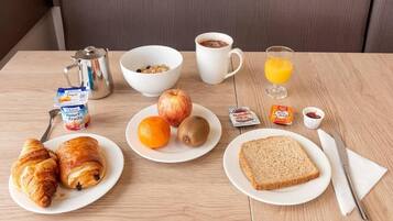 A breakfast table with croissants, fruits, a glass of orange juice, a coffee cup, and a butter packet.