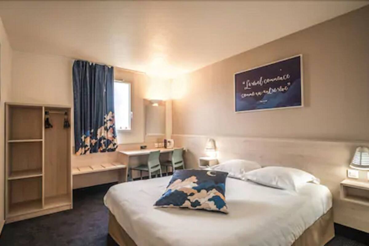 A hotel room with a bed, a desk, a chair, a wardrobe, and a mirror.