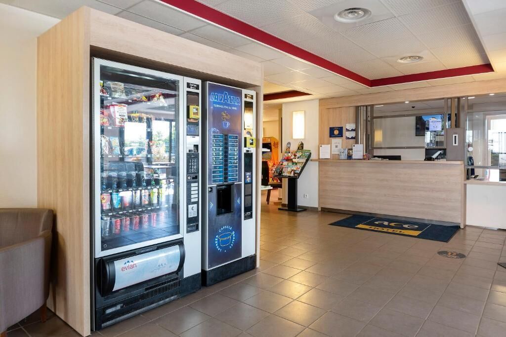 Un vestíbulo de hotel con mostrador de recepción, máquinas expendedoras y una pantalla digital.
