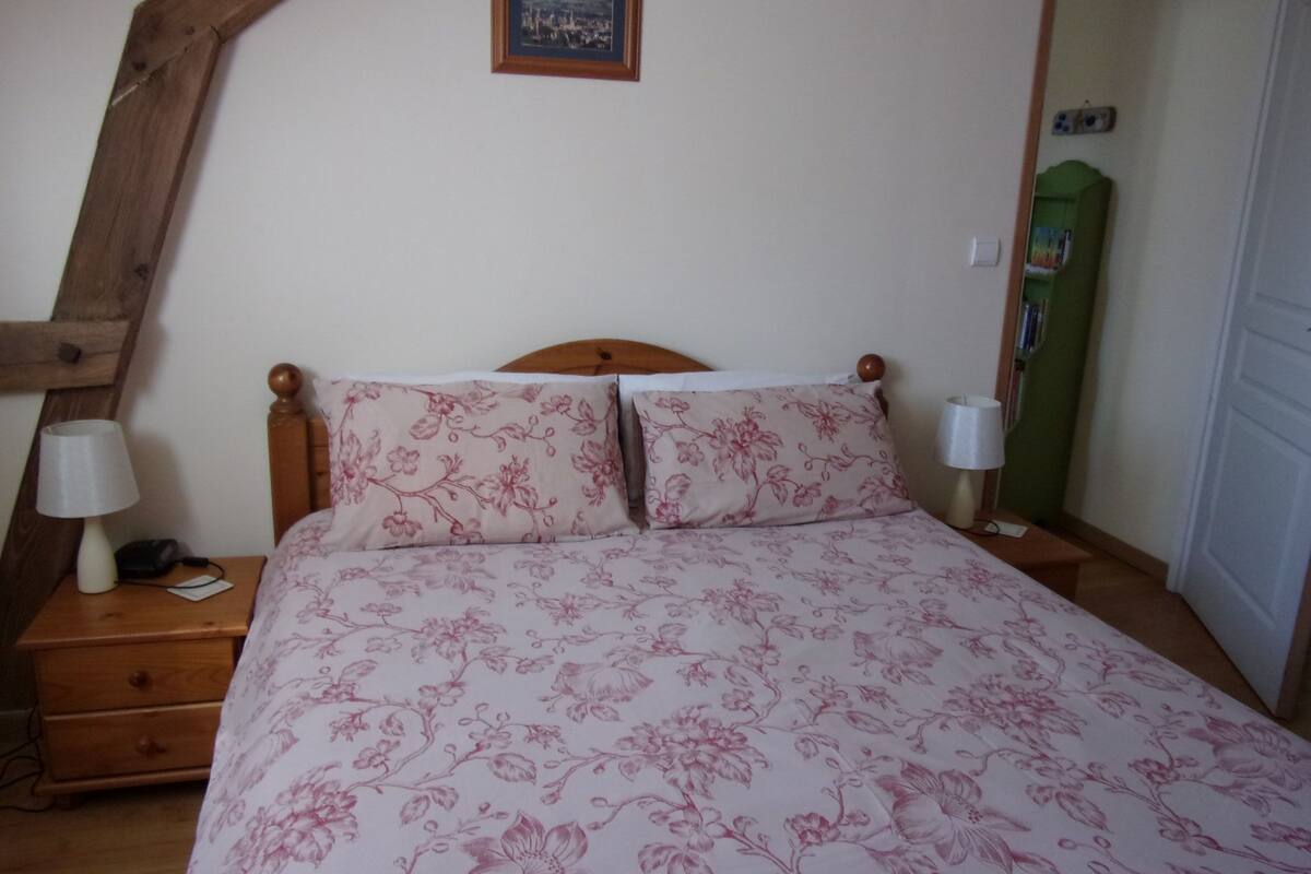 A bedroom with a wooden headboard, a bed with floral bedding, a nightstand with a lamp, and a framed picture on the wall.