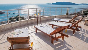 A terrace with wooden loungers, a table with drinks, and a view of the sea. - Apartments Raymond (Pržno)