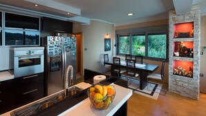 A modern kitchen with a built-in oven, a refrigerator with magnets, a dining area with a table and chairs, and a stone fireplace. - Apartments Raymond (Pržno)