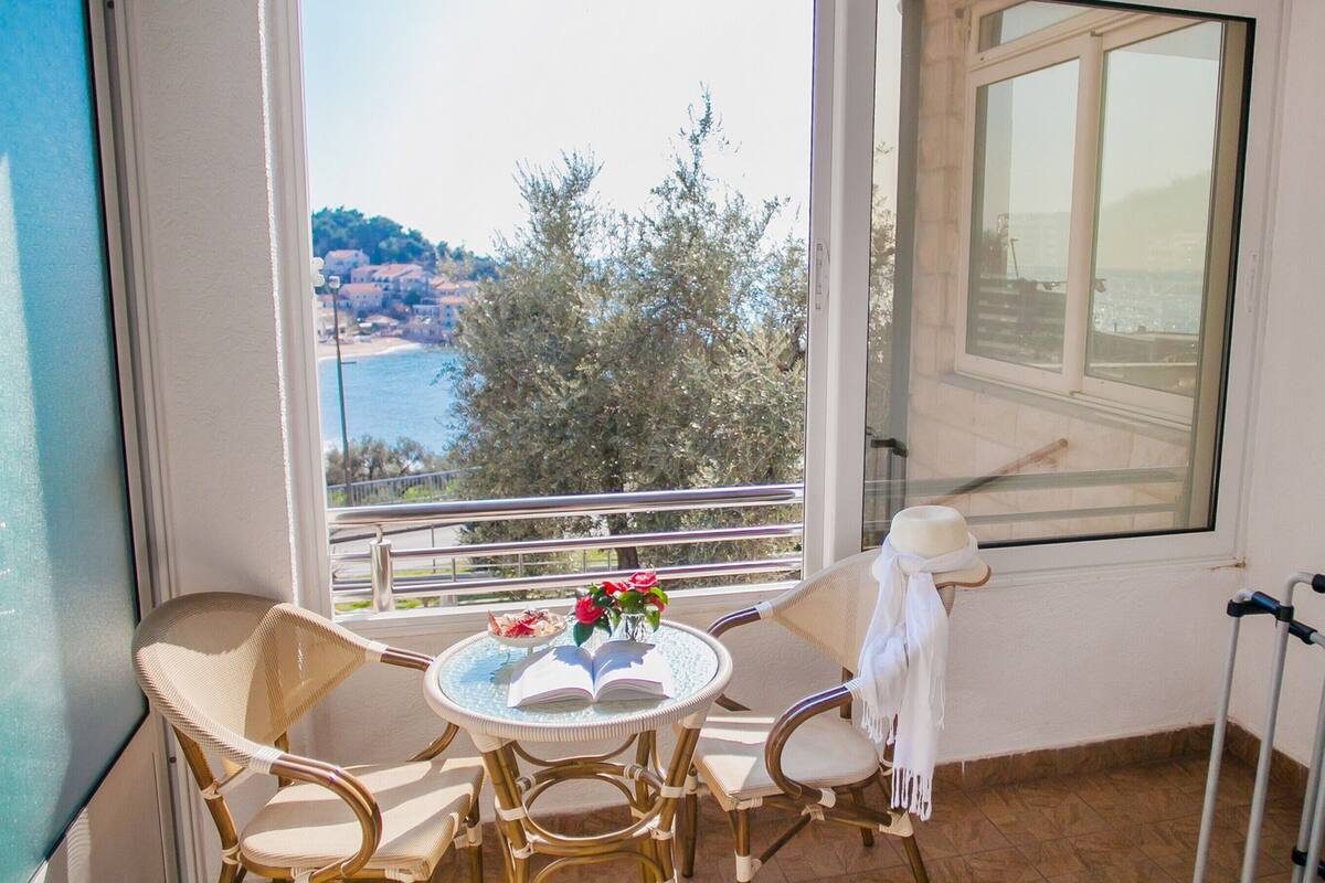 A balcony with wicker chairs, a small round table, and a view of a coastal town.