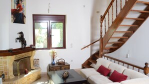 A living room with a fireplace, a sofa, a coffee table, and a wooden staircase. - Villa Bella Loukisia (Chalcis)