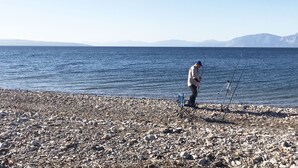 A rocky beach with a person fishing, a chair, and fishing rods. - Villa Bella Loukisia (Chalcis)