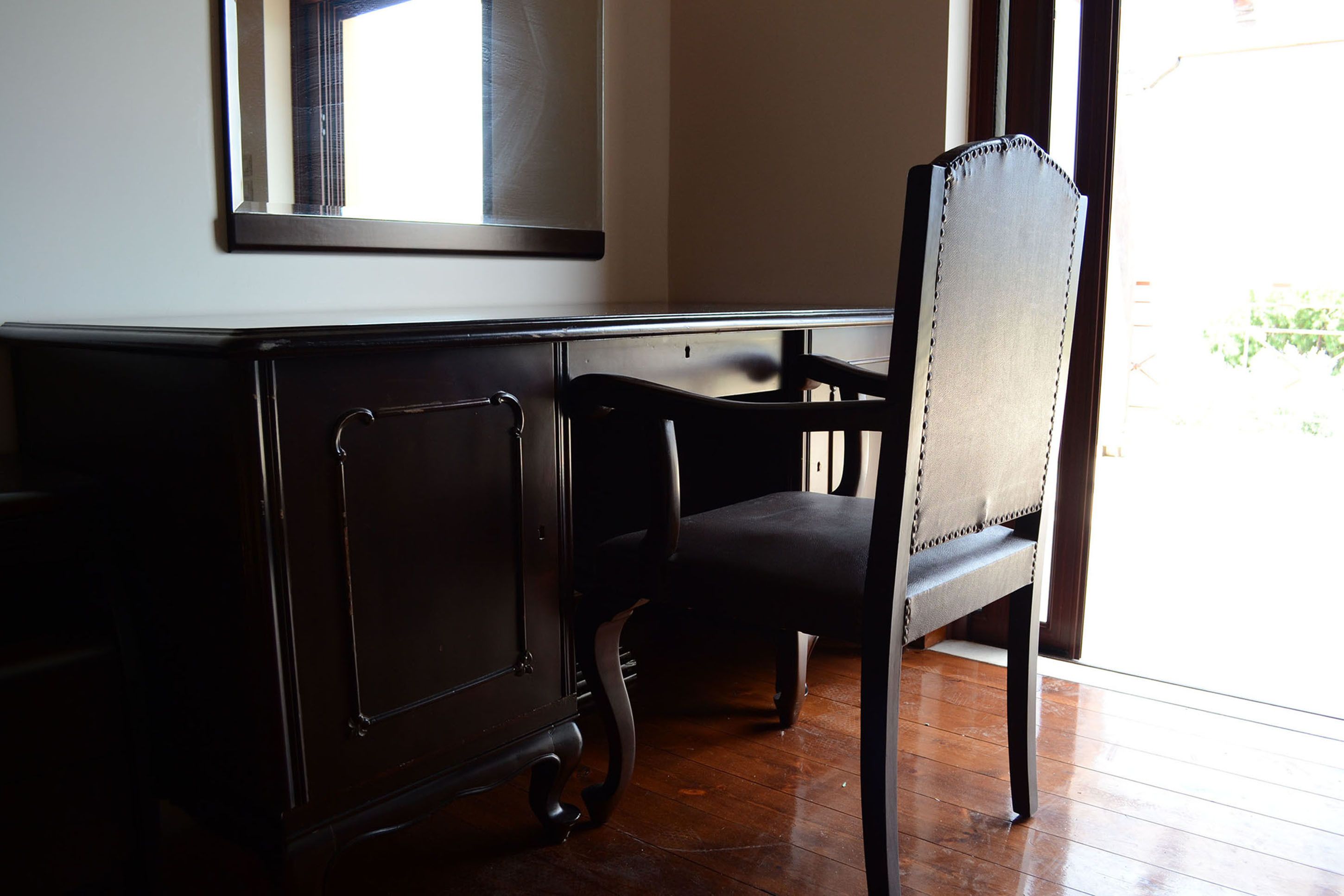 Una habitación con un escritorio de madera y una silla, una ventana con vistas y una puerta.